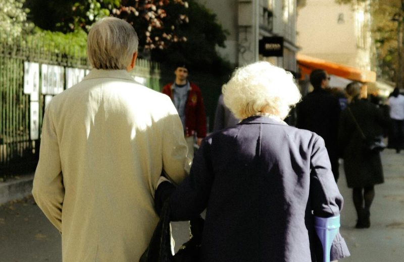 Aelteres Paar in der Stadt Arm in Arm — Rueckansicht